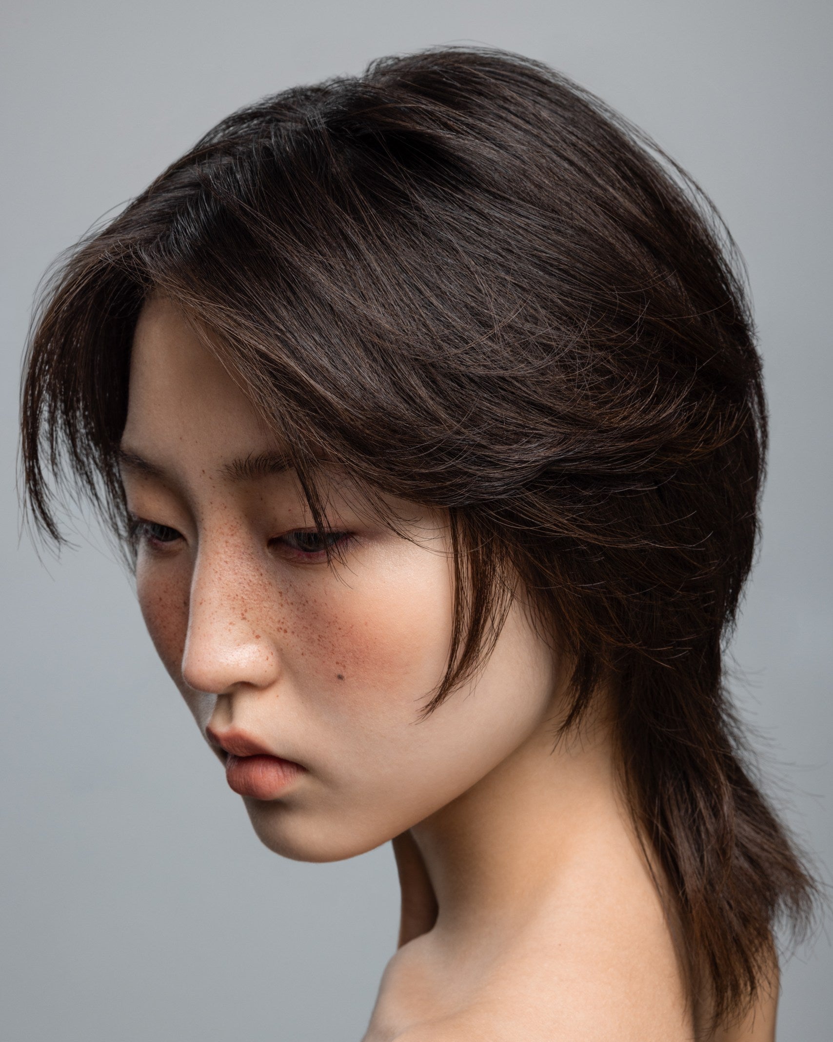 Profile portrait of a model with textured, luminous brown hair, showcasing the Plumeria hair care line by Yann Beyrie Paris against a neutral background.