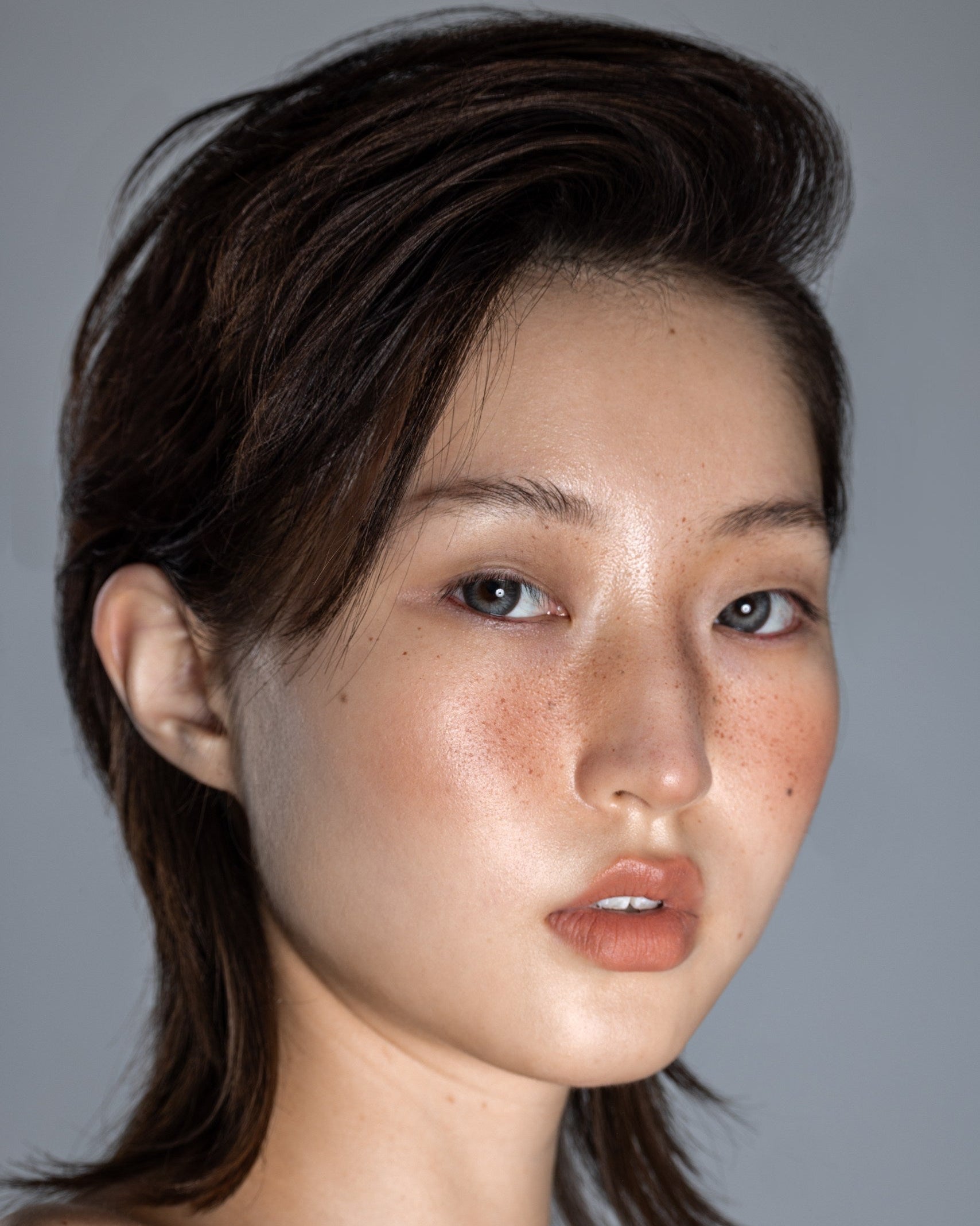 Close-up portrait of a model with voluminous textured hair and glowing skin, showcasing the Revitalising Water mist by Yann Beyrie Paris against a neutral background.