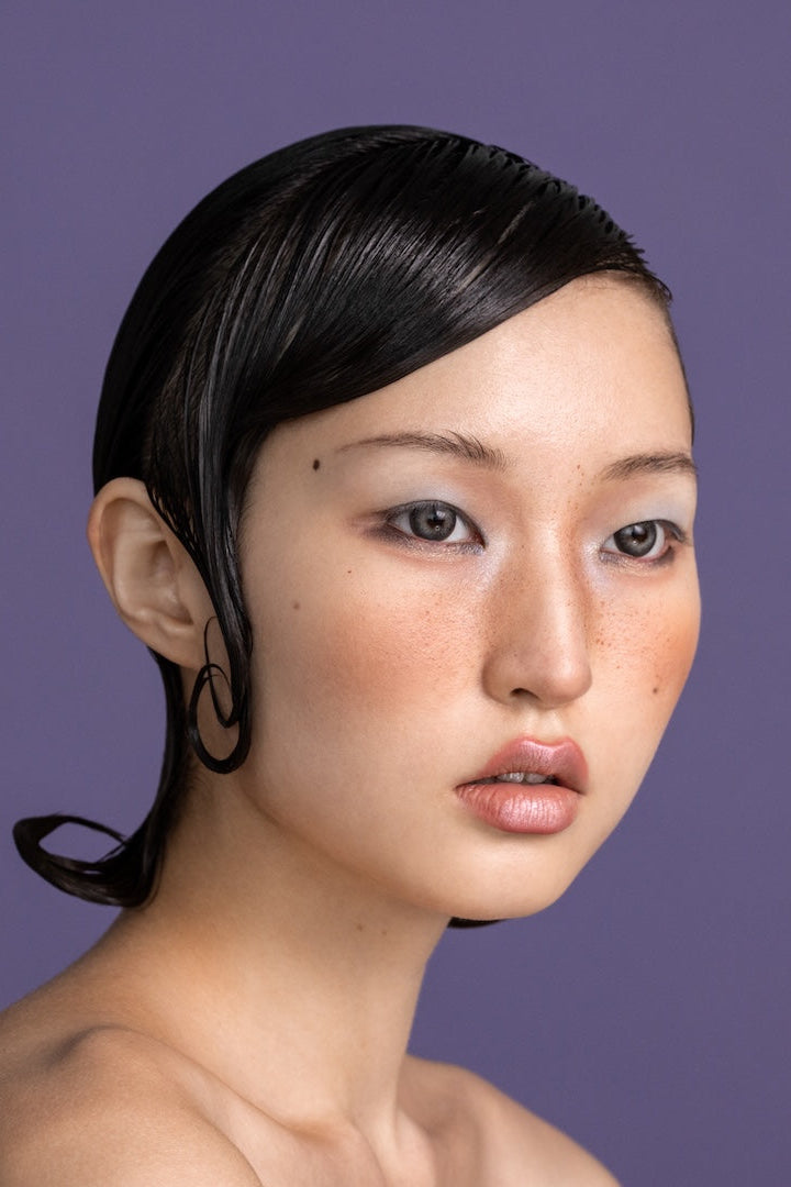 Asian female model with sleek sculpted dark hair and side wave on purple background for Yann Beyrie packages