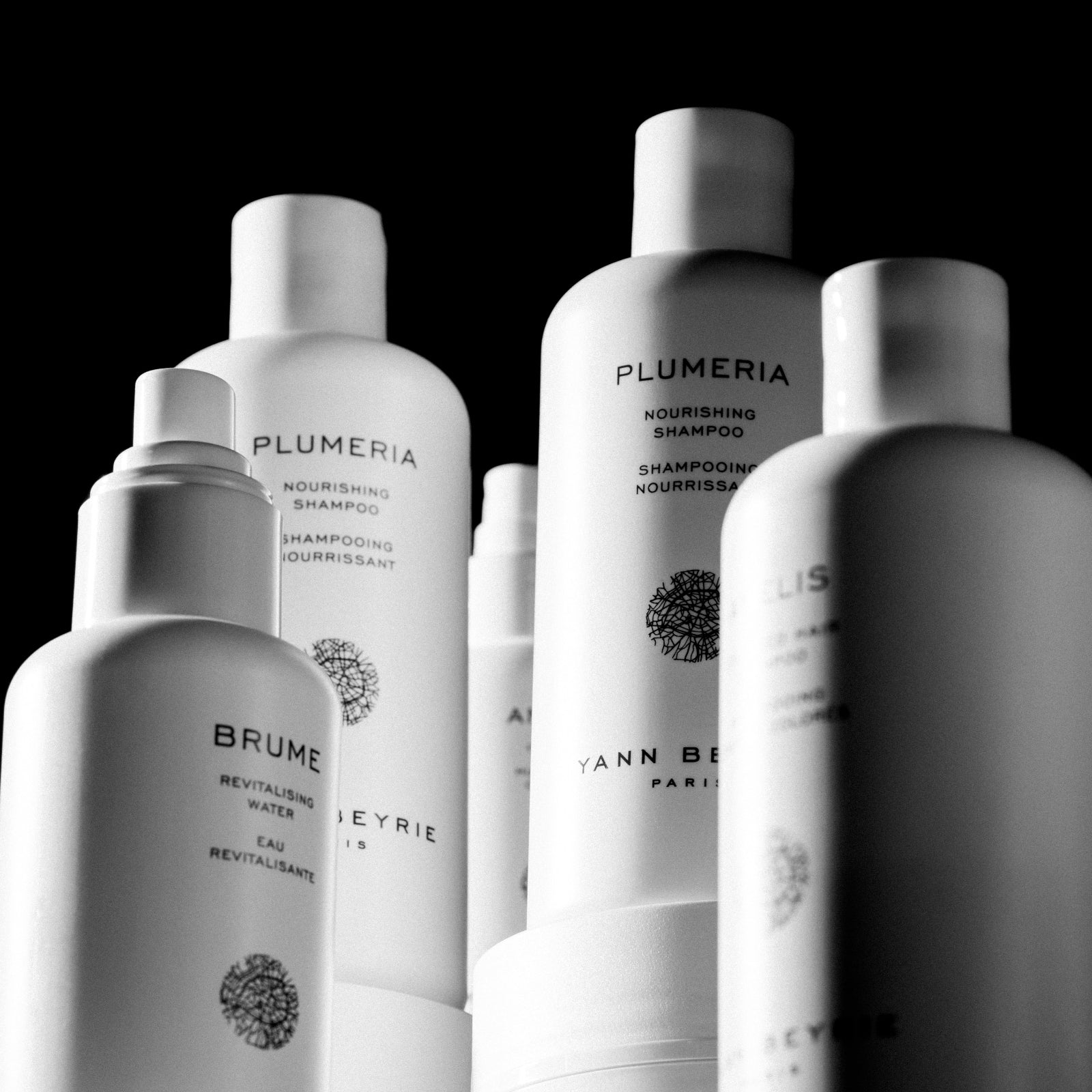 Black and white studio product lineup of Yann Beyrie Paris haircare range including Plumeria shampoo and Brume spray